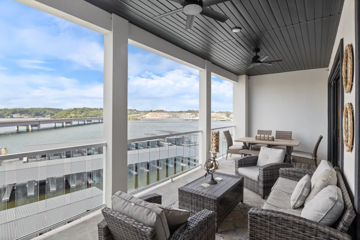 A calming exterior shot of a balcony with comfortable outdoor furniture and a dining table, looking directly onto a sweeping water view. The open-air setting beckons for quiet mornings or festive evenings, with the sense of privacy and connection to the water as key themes.