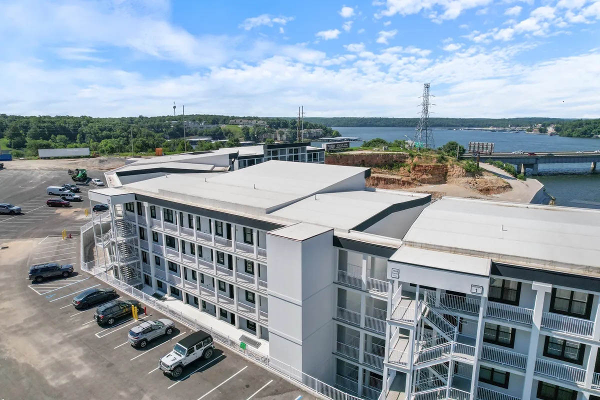 An exterior view of the building set against a waterfront background, with a parking lot in the foreground and natural landscaping. The scene invites guests to explore the outdoors and enjoy the scenic lakeside setting.