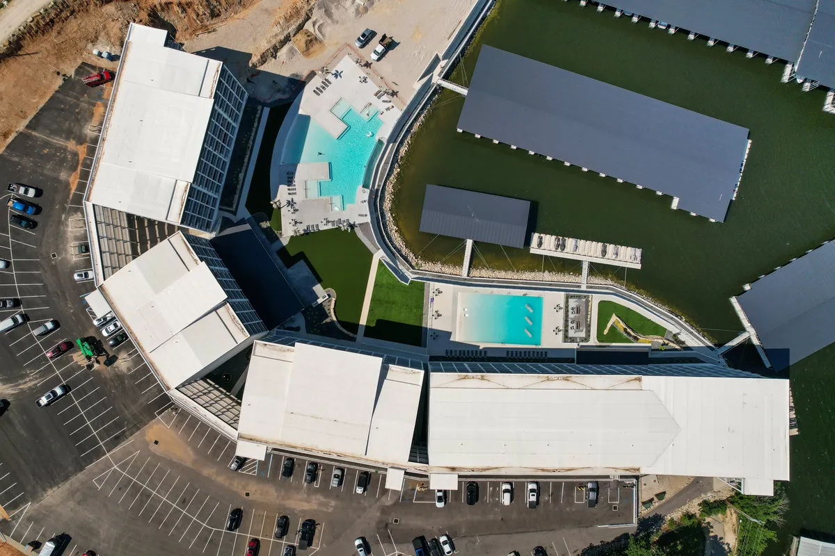 A vibrant exterior scene featuring a large swimming pool, surrounding buildings, ample lounging areas, and visible docks in the background—suggesting easy access to water activities and boat slips. The overall atmosphere is lively yet relaxed, perfect for group gatherings.