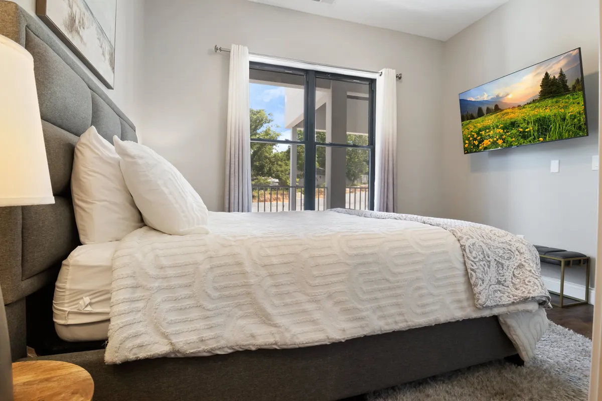 A comfortable bedroom with plush bedding, a large window streaming in natural light, and a wall-mounted TV. The atmosphere is relaxed and cozy, perfect for unwinding after a day of lakeside adventures.
