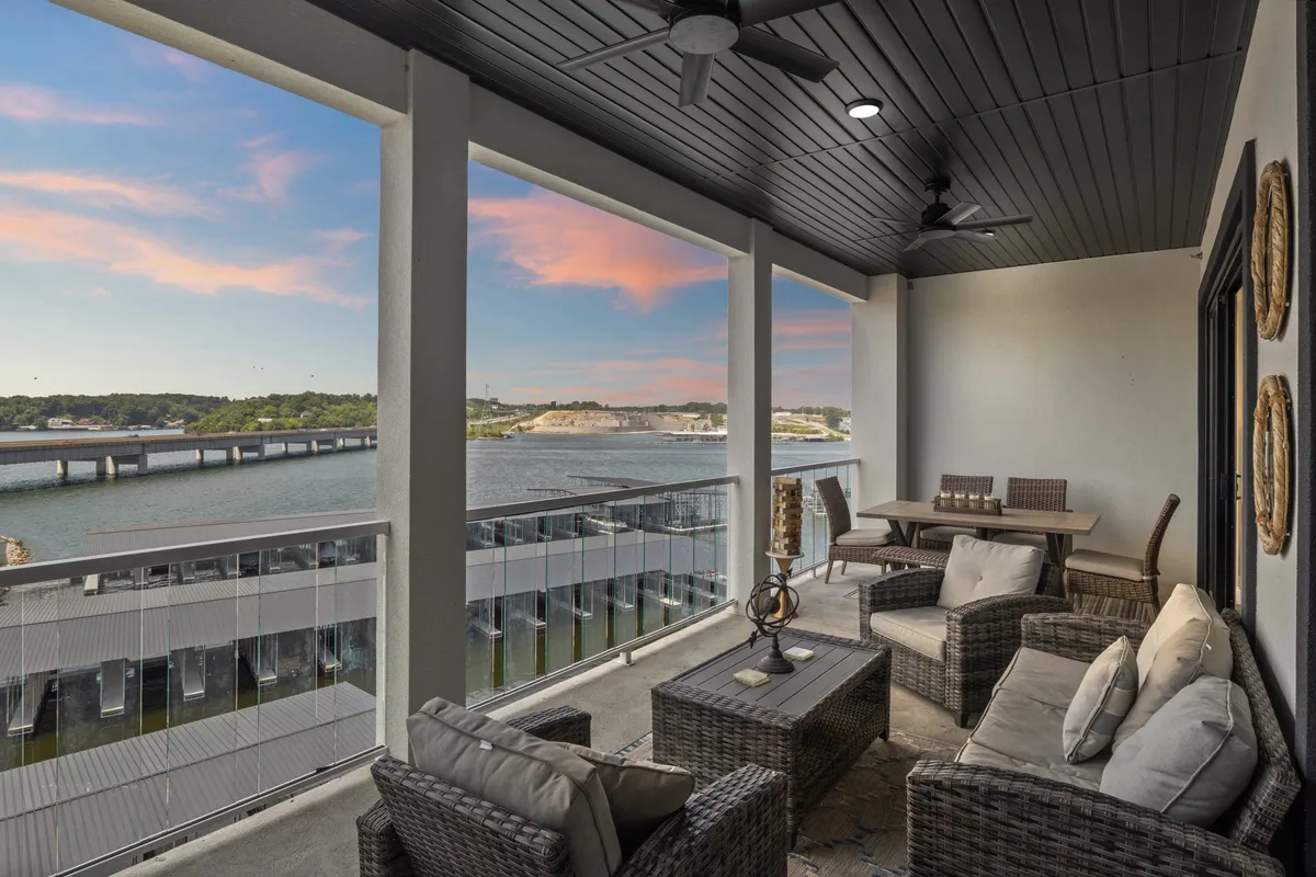 The image showcases the condo's private outdoor seating area, perfectly positioned to overlook the glistening lake at sunset. Plush chairs encircle a cozy dining table, inviting guests to relax, dine, and soak in the breathtaking views as evening falls. The vibrant colors of the sunset sky reflect on the water, creating a tranquil and memorable setting.
