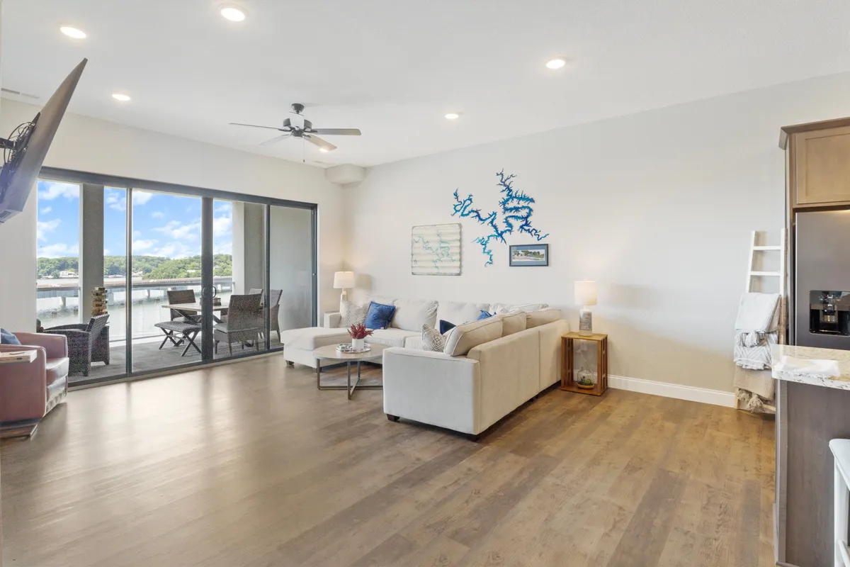 A modern living room with a large sectional sofa and expansive windows overlooking the water. Artistic wall decor and contemporary furnishings create a warm, welcoming atmosphere ideal for relaxing or hosting friends, while the lake view connects the interior with the outdoors.