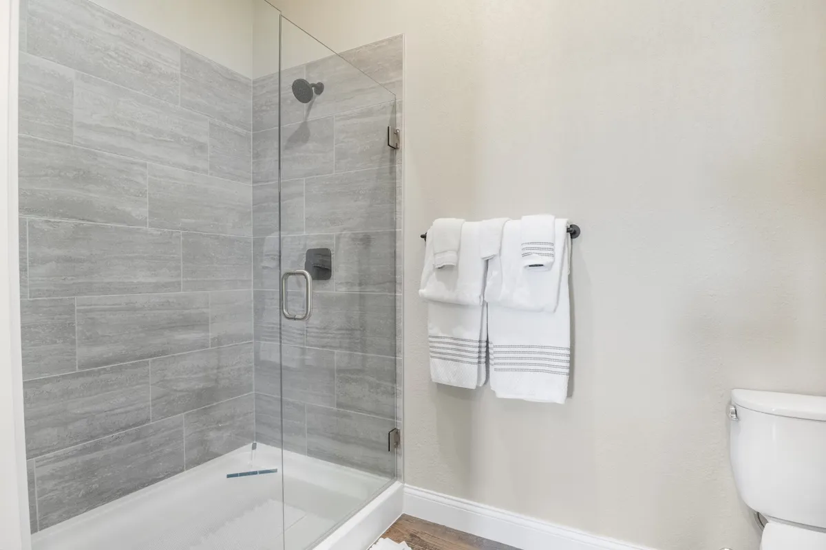 This image presents an en suite bathroom with a glass shower enclosure, neatly arranged towels, and modern fixtures. The room feels fresh, inviting, and designed for relaxation and self-care.