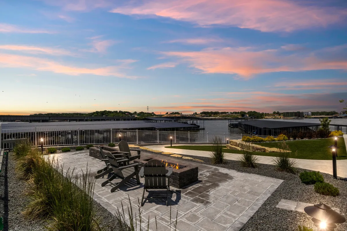 A tranquil fire pit area with Adirondack chairs arranged around the fire, backed by a stunning waterfront view and a sky painted with sunset colors. It invites groups to gather and enjoy the peaceful lakeside setting.