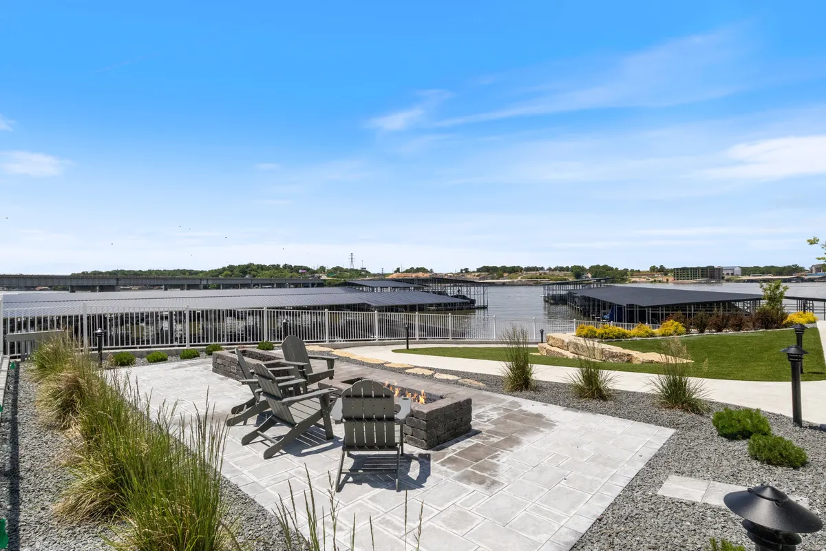 A tranquil waterfront setting featuring a stone fire pit surrounded by comfortable seating, situated right by the lake. Lush landscaping and calm waters provide a relaxing backdrop—ideal for picnics, cookouts, or gathering for evening fireside chats after a day of adventure.