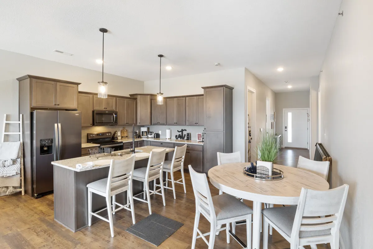 A stylish kitchen with a prominent island, adjacent to a welcoming dining table. The atmosphere is social and inviting, designed for family dinners, shared recipes, and gatherings. Ample cabinetry and a modern refrigerator make it both practical and appealing.
