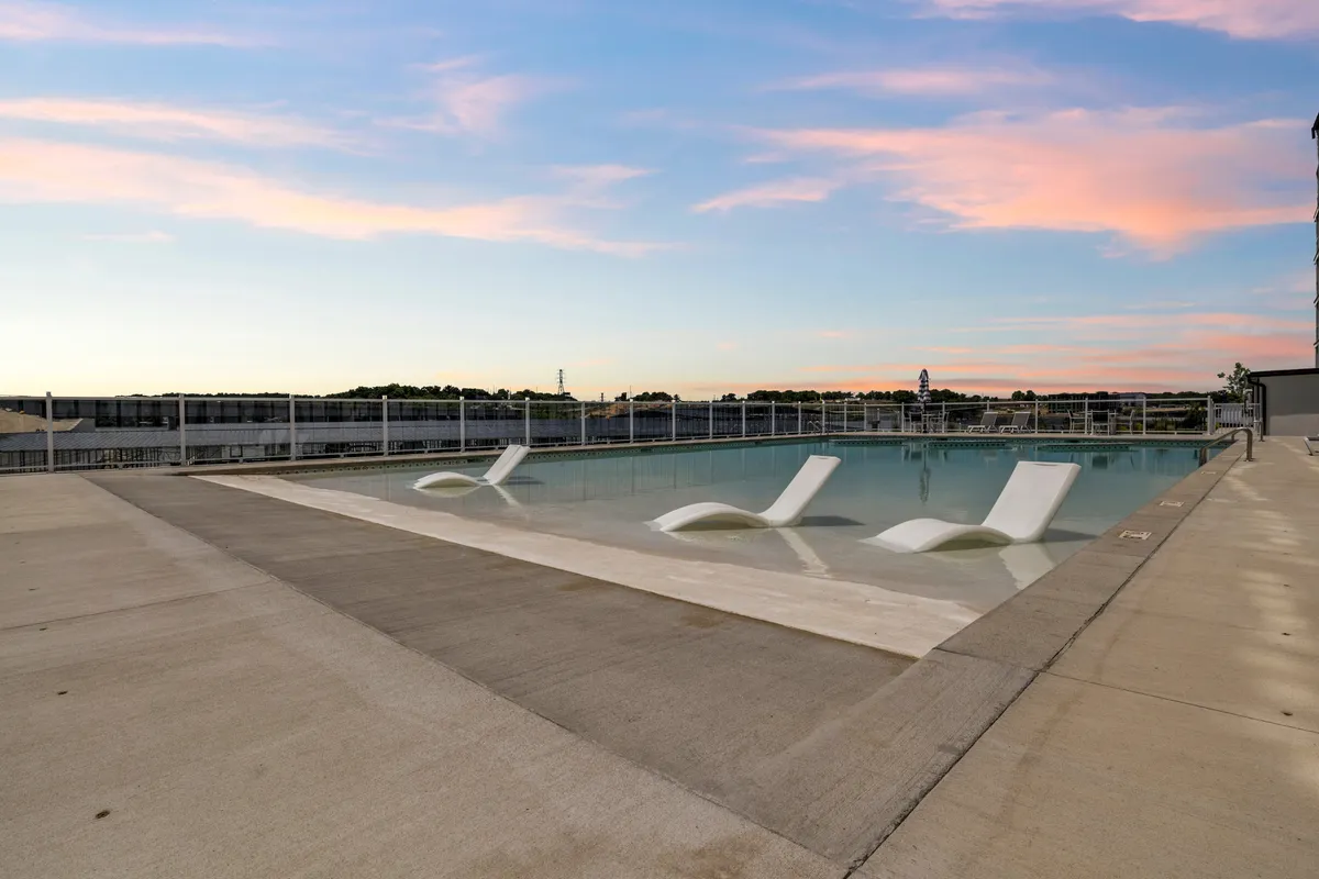 An inviting outdoor swimming pool bordered by comfortable lounge chairs and set beneath a wide-open sky. The serene setting is perfect for both energetic kids and adults looking to unwind, with ample space for swimming, sunbathing, and socializing.
